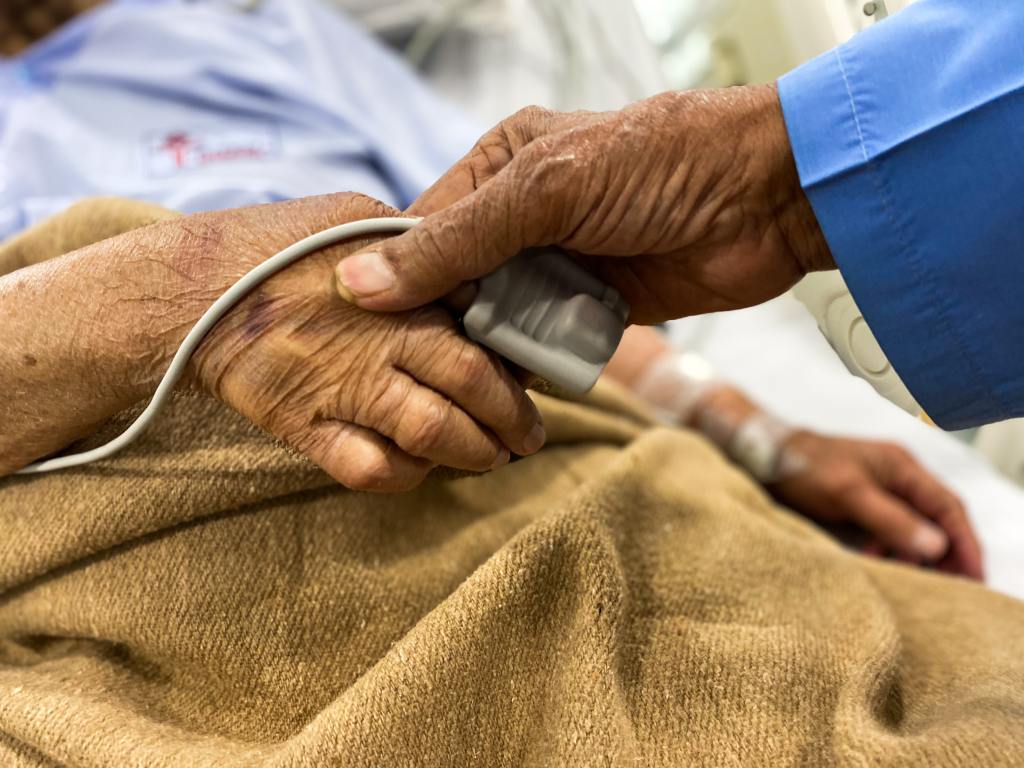 Photo of a healthcare worker holding the hand of an older patient in hosptial